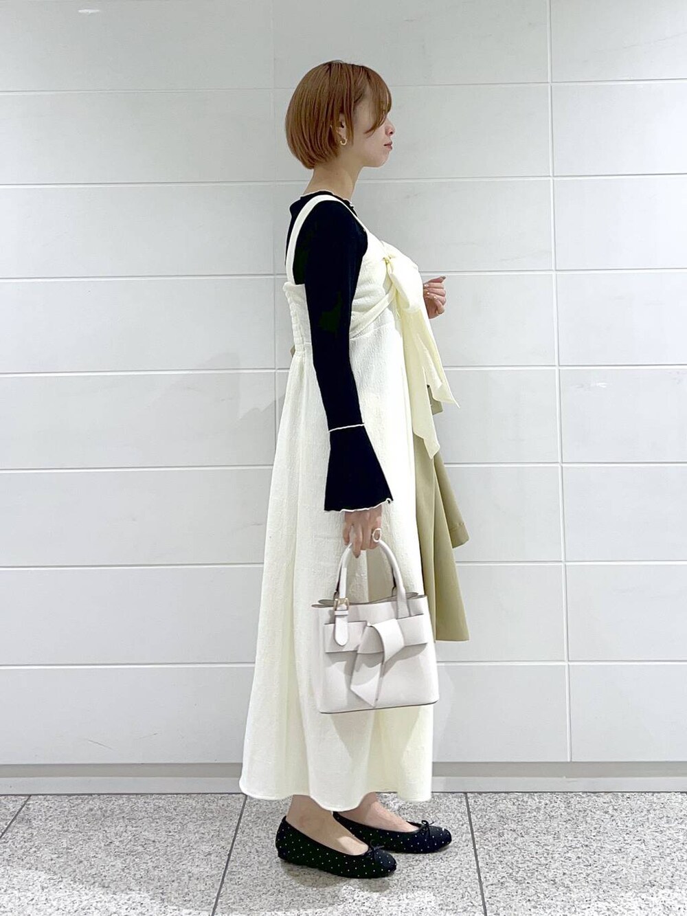 ホワイト系のショルダーバッグ、ベージュ系のトレンチコート、ブラック系のバレエシューズを着用したレディースの春コーディネートの5枚目の写真