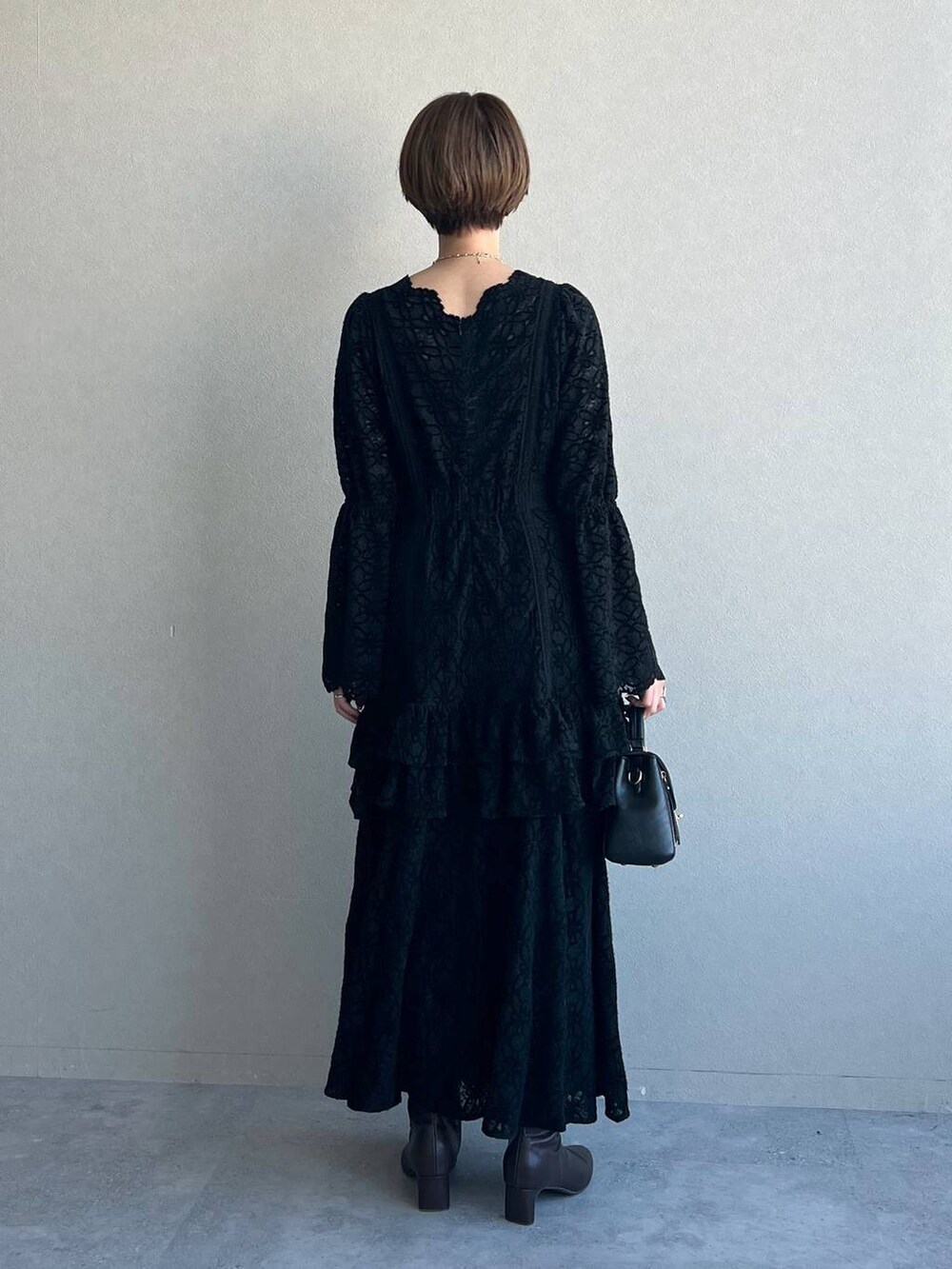 ブラック系のワンピース、パープル系のチェスターコート、ブラック系のブーツを着用したレディースの冬コーディネートの6枚目の写真