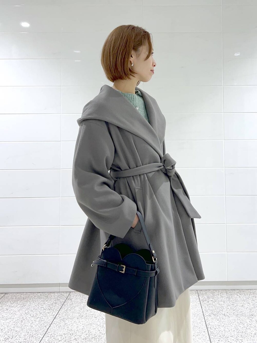 グレー系のノーカラーコート、ブラック系のショルダーバッグ、ブラック系のブーツを着用したレディースの秋コーディネートの4枚目の写真