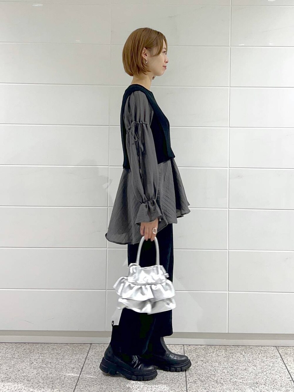 シルバー系のショルダーバッグ、ブラック系のブーツ、ブラック系のスカートを着用したレディースの秋コーディネートの6枚目の写真