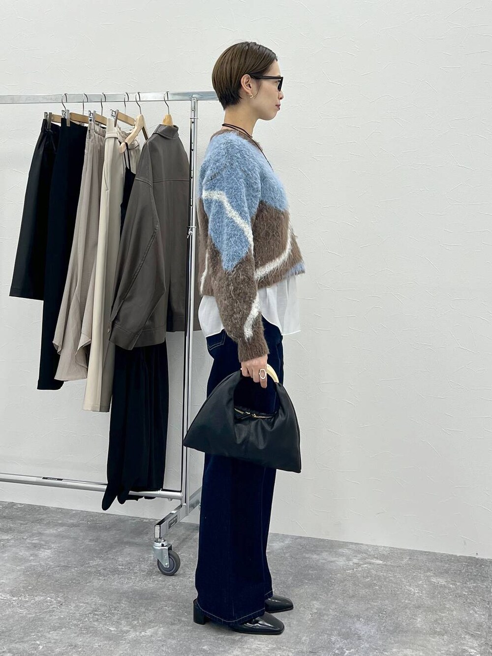 ブラウン系のニット/セーター、ブラック系のハンドバッグ、ブルー系のデニムパンツを着用したレディースの秋コーディネートの3枚目の写真