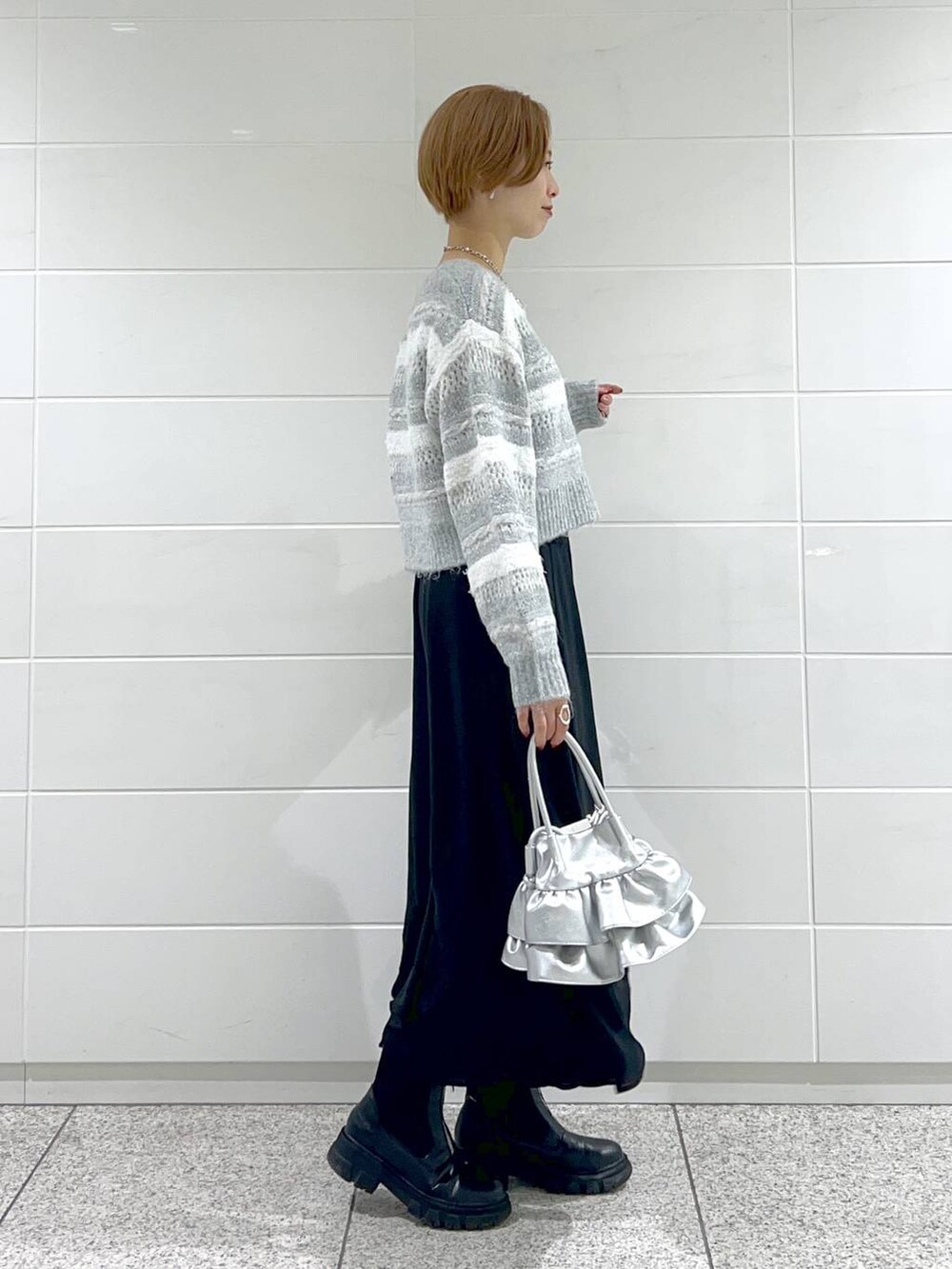 シルバー系のショルダーバッグ、ブラック系のブーツ、ブラック系のスカートを着用したレディースの冬コーディネートの2枚目の写真