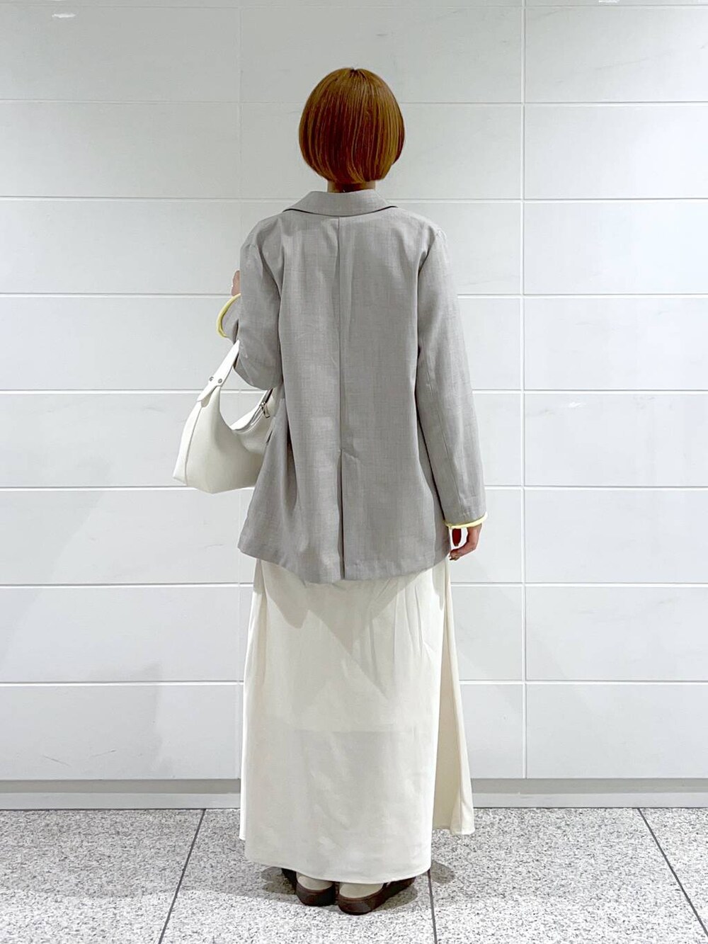 イエロー系のニット/セーター、グレー系のテーラードジャケット、ホワイト系のスカートを着用したレディースの春コーディネートの3枚目の写真