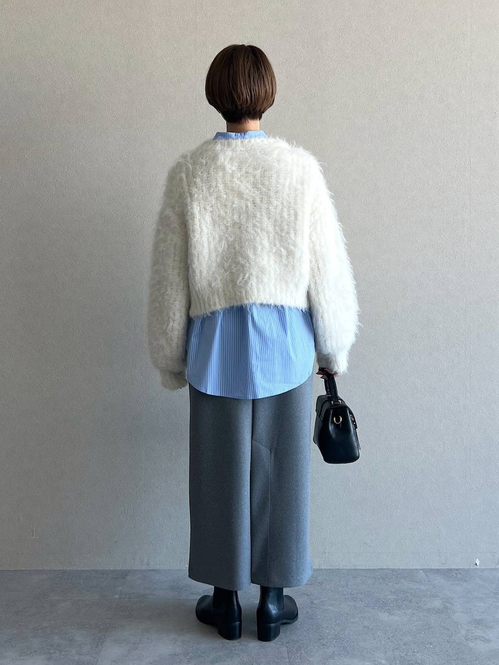 グレー系のスカート、ブラック系のブーツ、ホワイト系のニット/セーターを着用したレディースの冬コーディネートの3枚目の写真