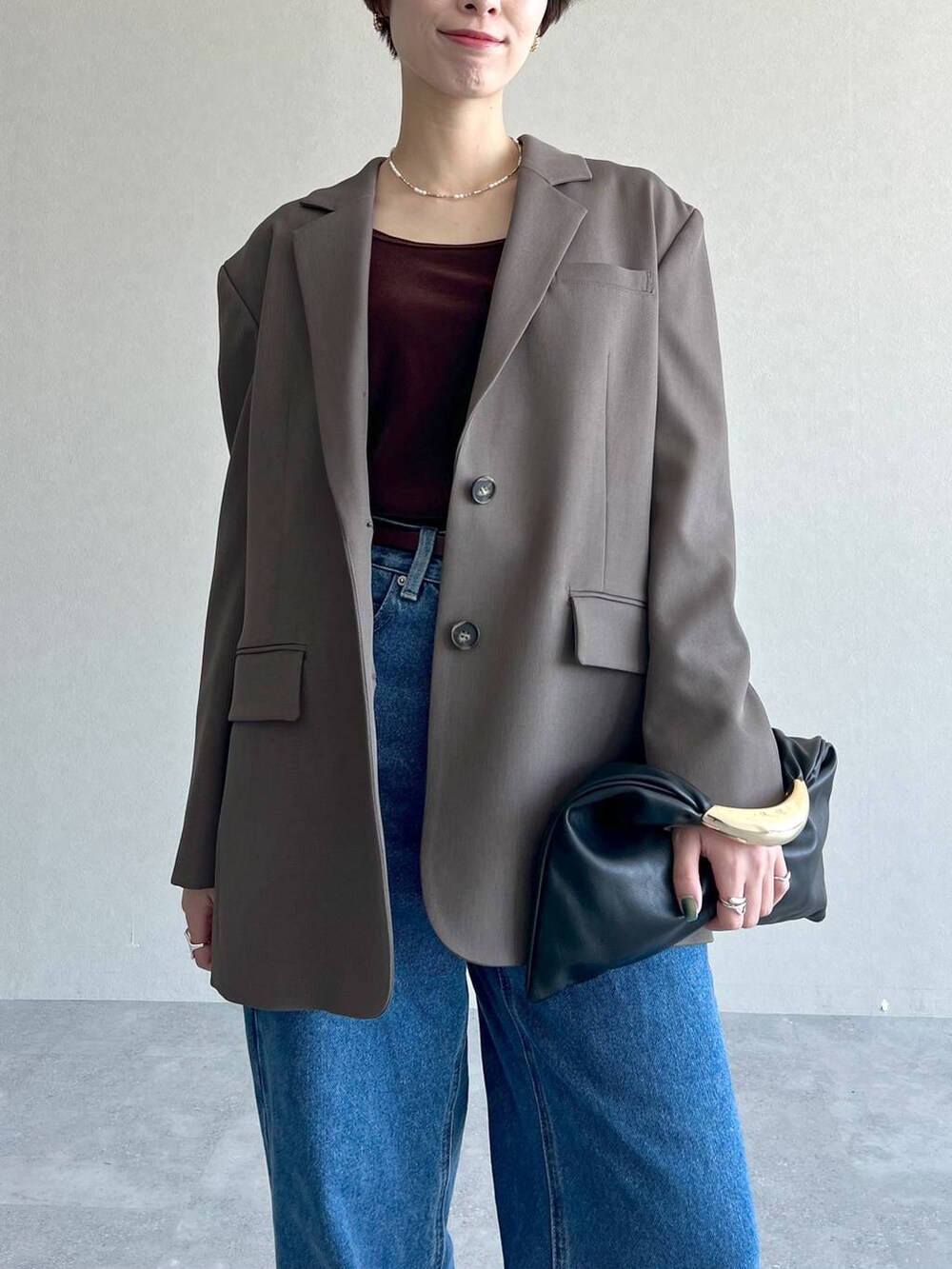 ブラック系のハンドバッグ、ブラウン系のテーラードジャケット、ブルー系のデニムパンツを着用したレディースの秋コーディネートの4枚目の写真