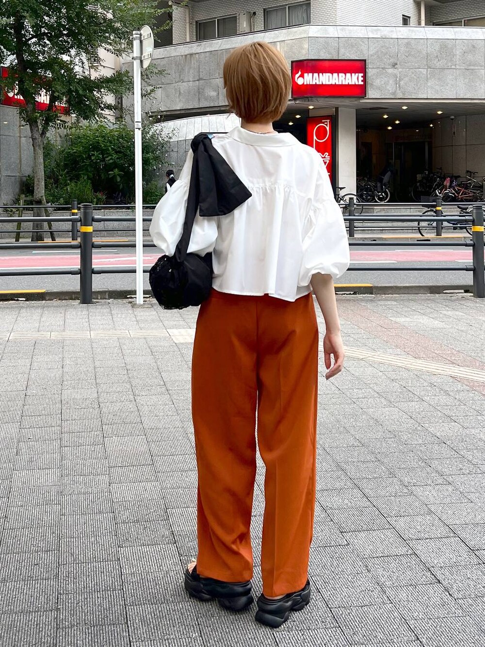 ブラック系のショルダーバッグ、ホワイト系のシャツ/ブラウス、オレンジ系のスラックスを着用したレディースの秋コーディネートの3枚目の写真