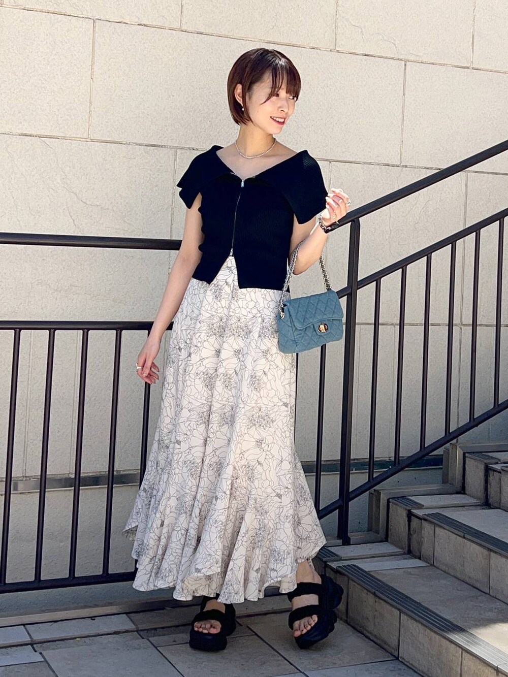 ブラック系のニット/セーター、ブルー系のショルダーバッグ、ホワイト系のスカートを着用したレディースの夏コーディネートの2枚目の写真