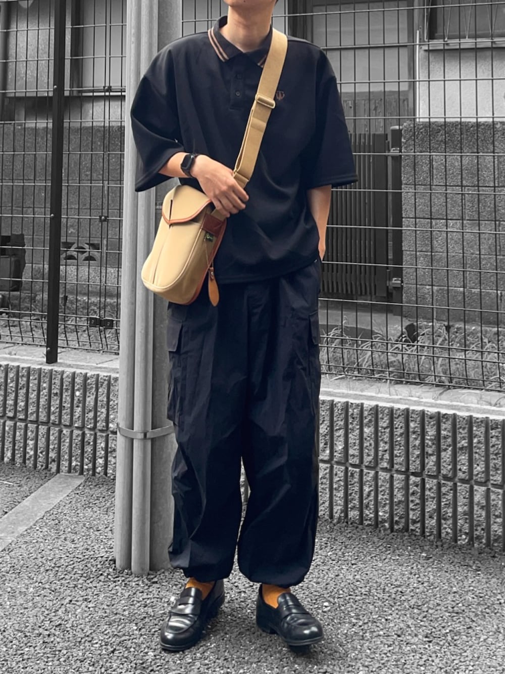 ブラック系のポロシャツ、ベージュ系のショルダーバッグ、ブラック系のカーゴパンツを着用したメンズの夏コーディネートの3枚目の写真