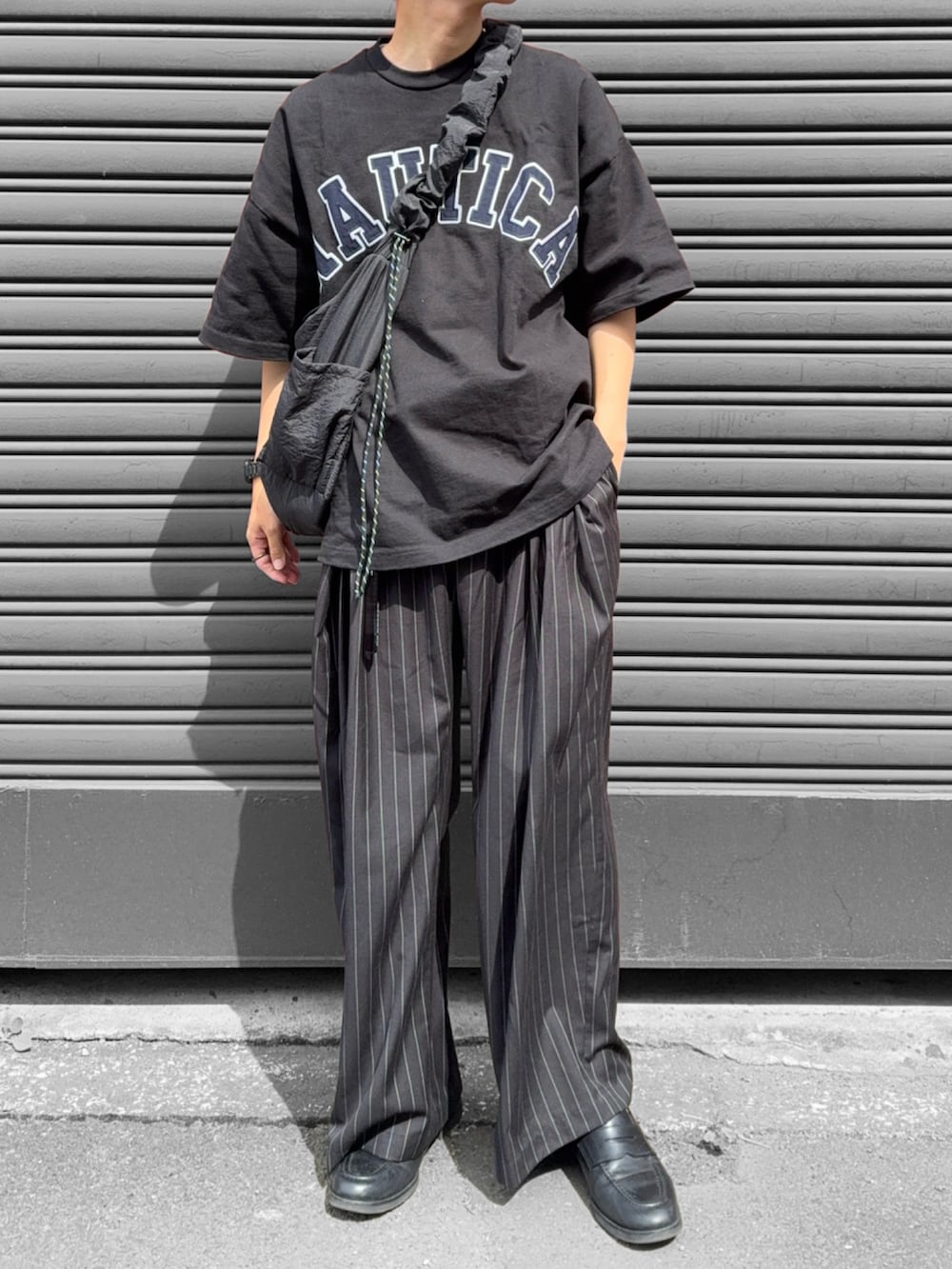 ブラック系のショルダーバッグ、ブラック系のスラックス、ブラック系のローファーを着用したメンズの夏コーディネートの2枚目の写真