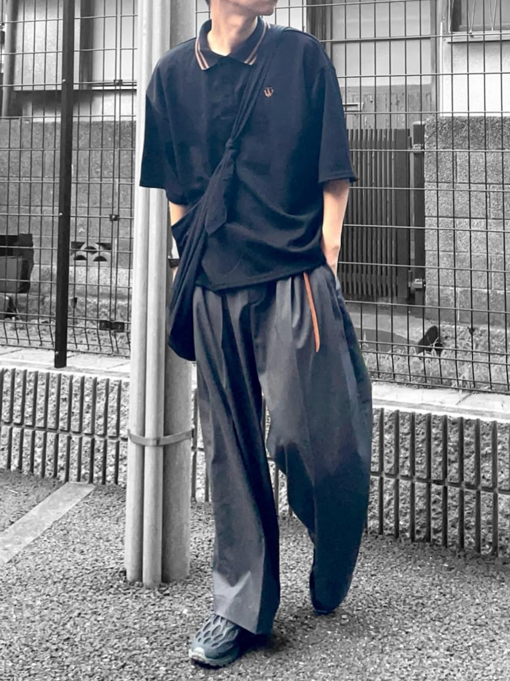 ブラック系のポロシャツ、ブラック系のショルダーバッグ、グレー系のスラックスを着用したメンズの夏コーディネートの2枚目の写真