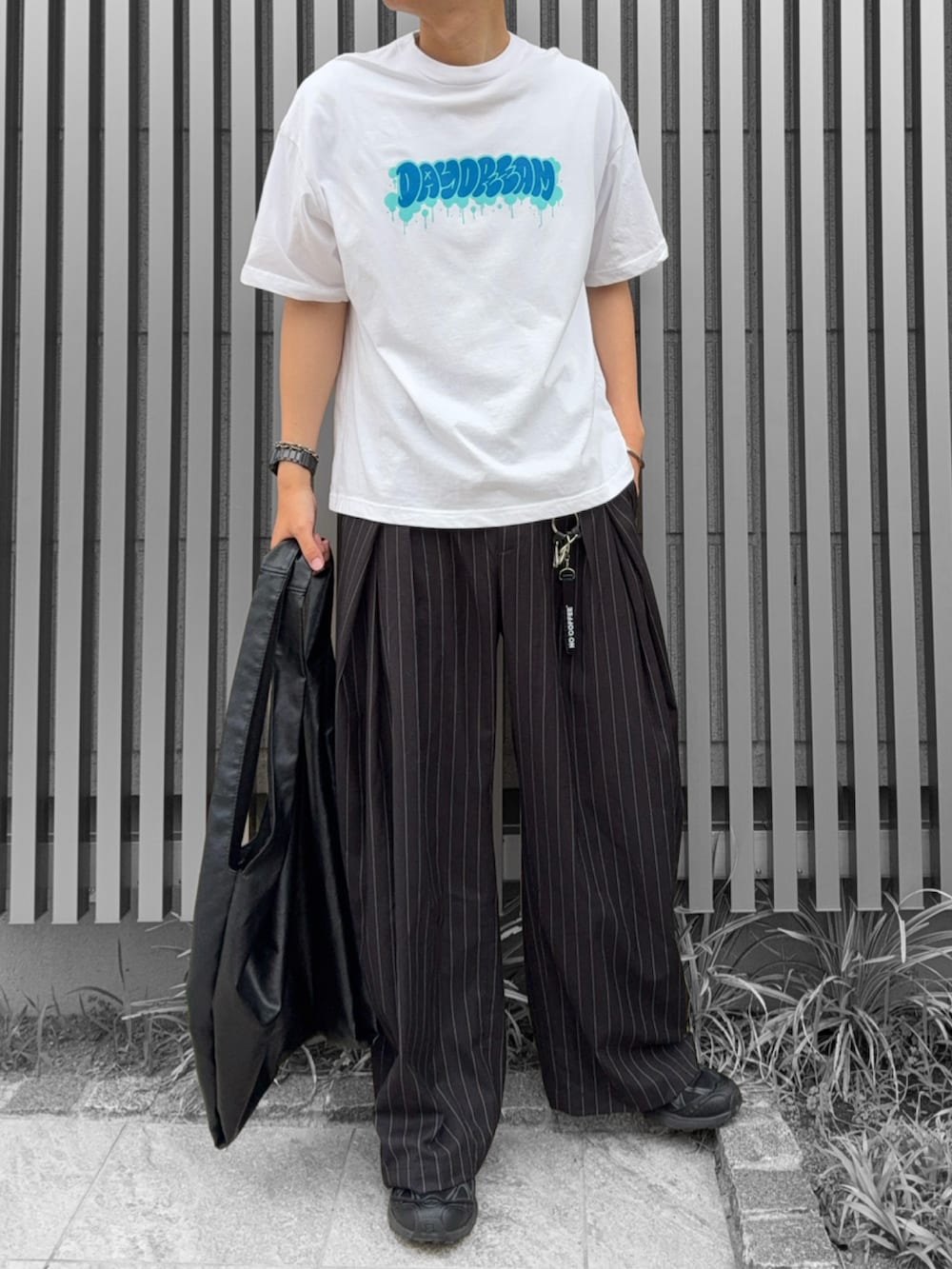 ブラック系のトートバッグ、ブラック系のスラックス、ホワイト系のTシャツ/カットソーを着用したメンズの夏コーディネートの2枚目の写真