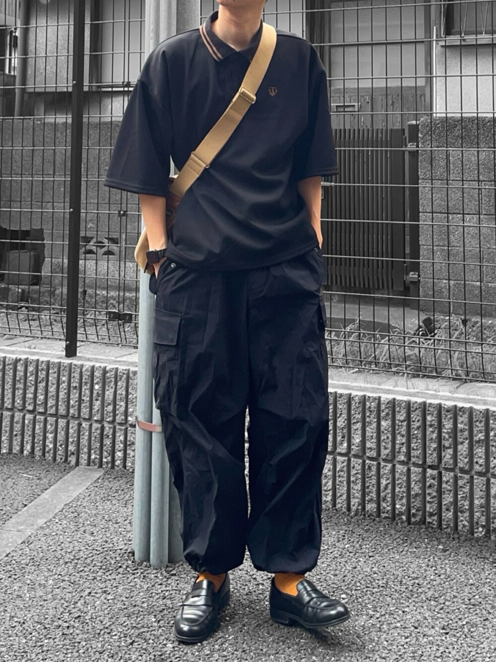 ブラック系のポロシャツ、ベージュ系のショルダーバッグ、ブラック系のカーゴパンツを着用したメンズの夏コーディネートの2枚目の写真