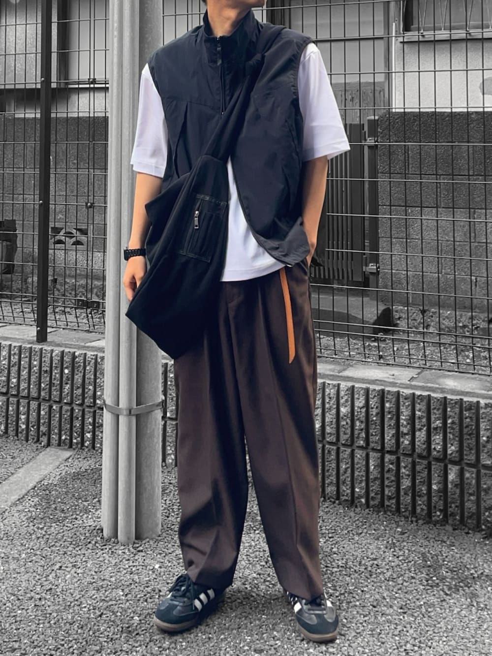 ブラック系のベスト、ブラック系のショルダーバッグ、ブラウン系のスラックスを着用したメンズの夏コーディネートの2枚目の写真