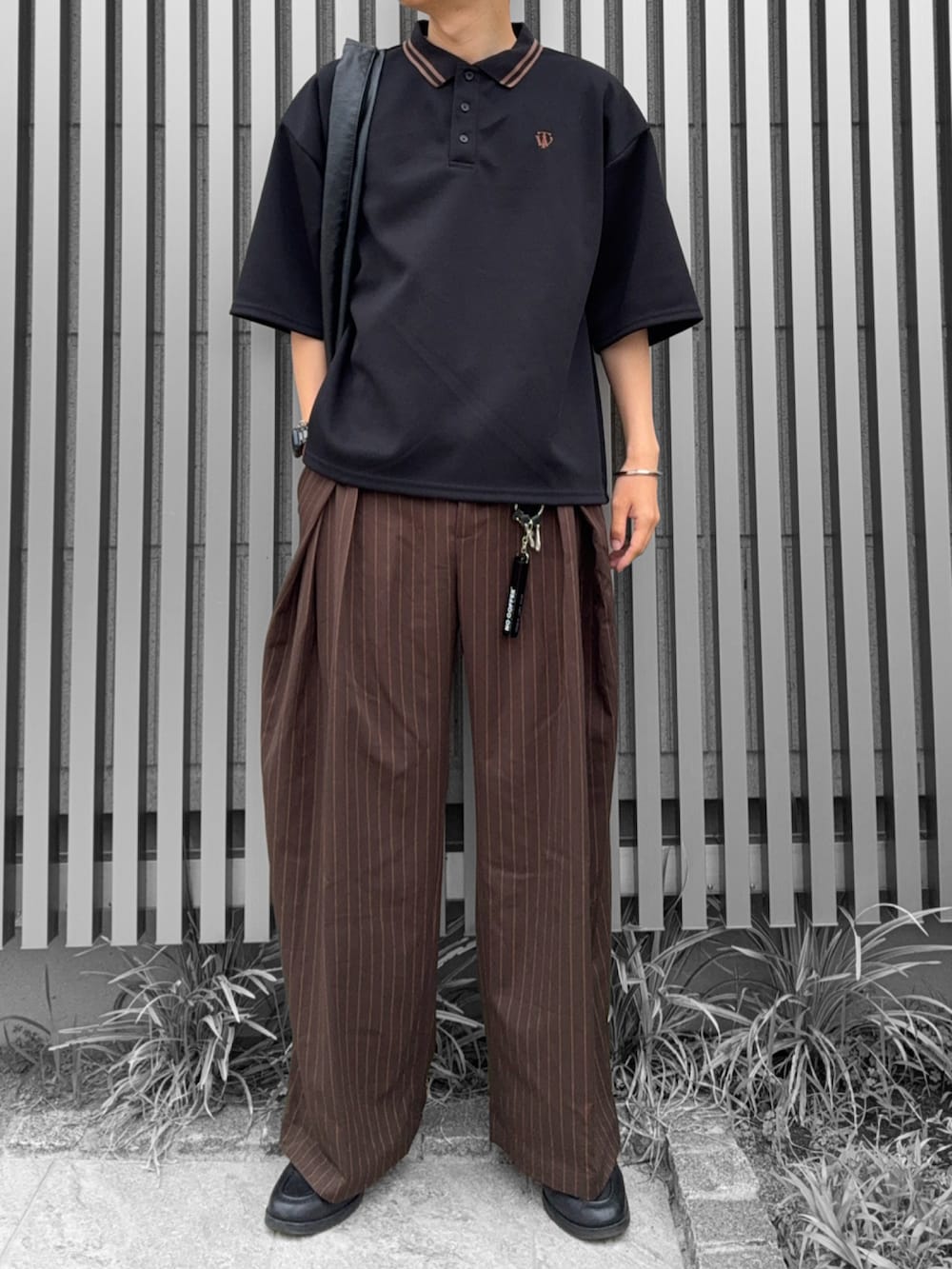 ブラック系のトートバッグ、ブラック系のポロシャツ、ブラウン系のスラックスを着用したメンズの夏コーディネートの2枚目の写真