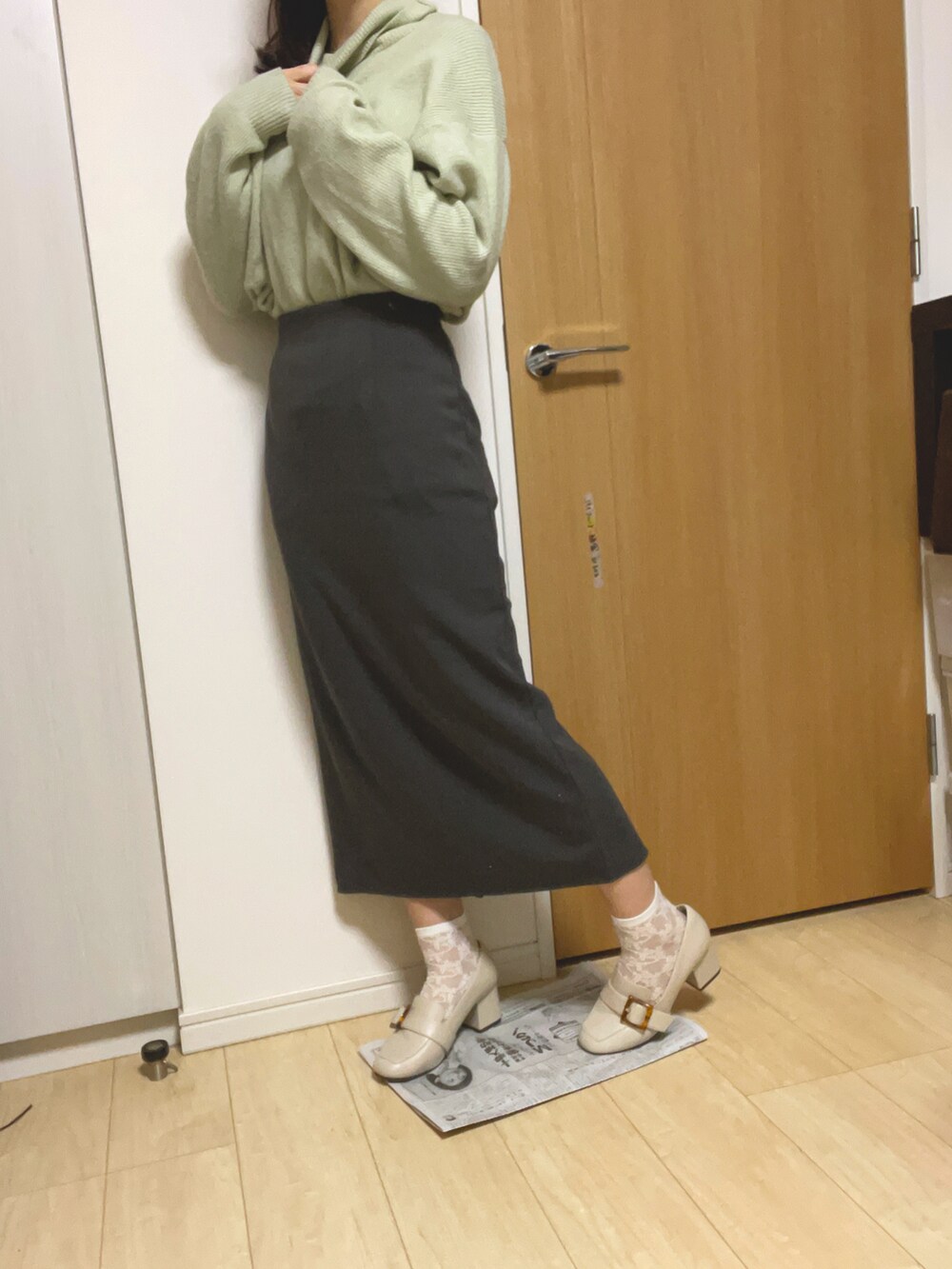 グレー系のスカート、グリーン系のニット/セーター、ホワイト系のパンプスを着用したレディースの冬コーディネートの2枚目の写真