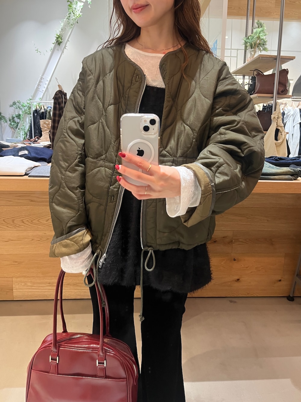 レッド系のボストンバッグ、グリーン系のブルゾン、ホワイト系のTシャツ/カットソーを着用したレディースの秋コーディネートの2枚目の写真