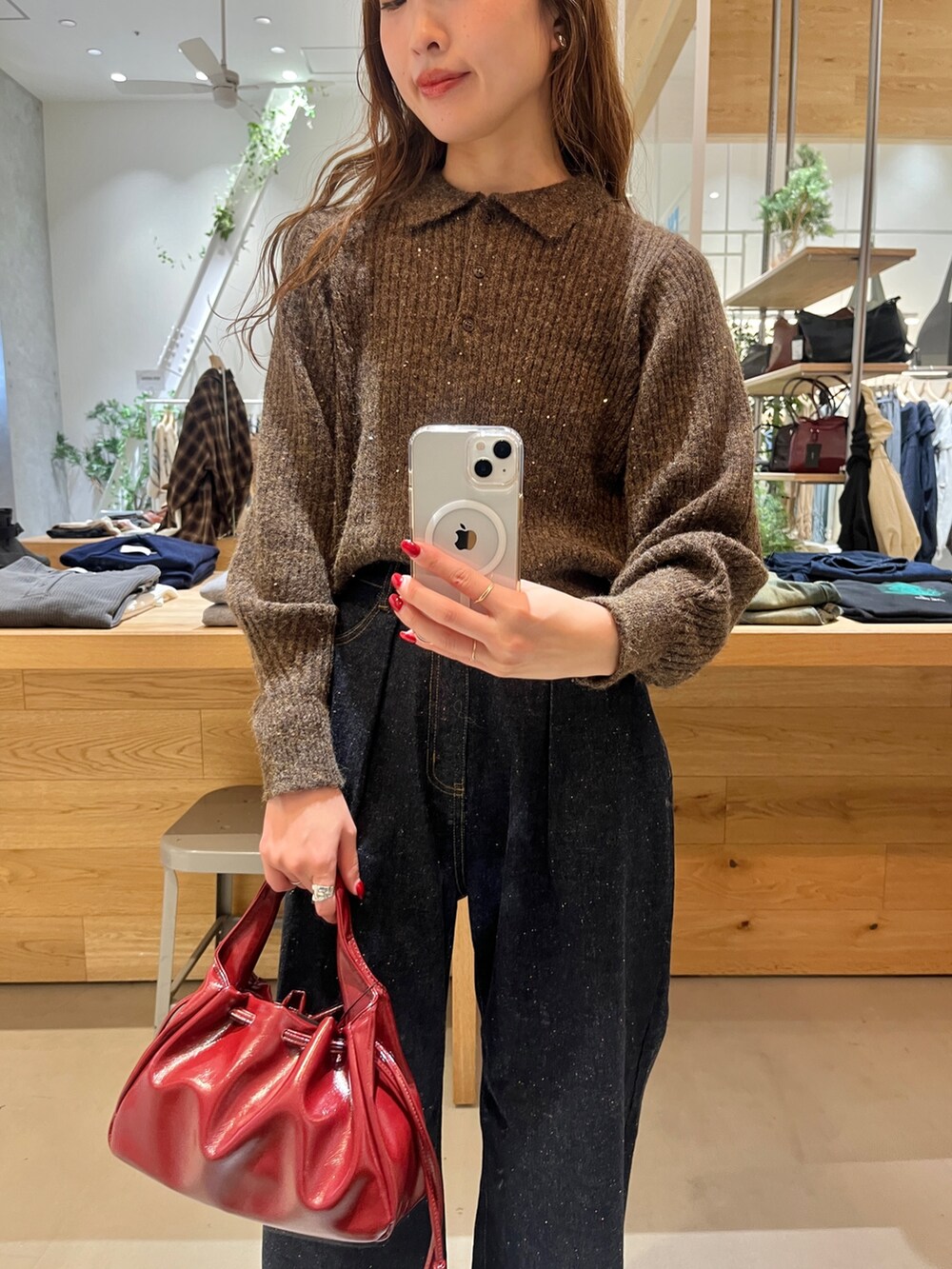 レッド系のショルダーバッグ、ブルー系のデニムパンツ、ブラウン系のニット/セーターを着用したレディースの秋コーディネートの2枚目の写真