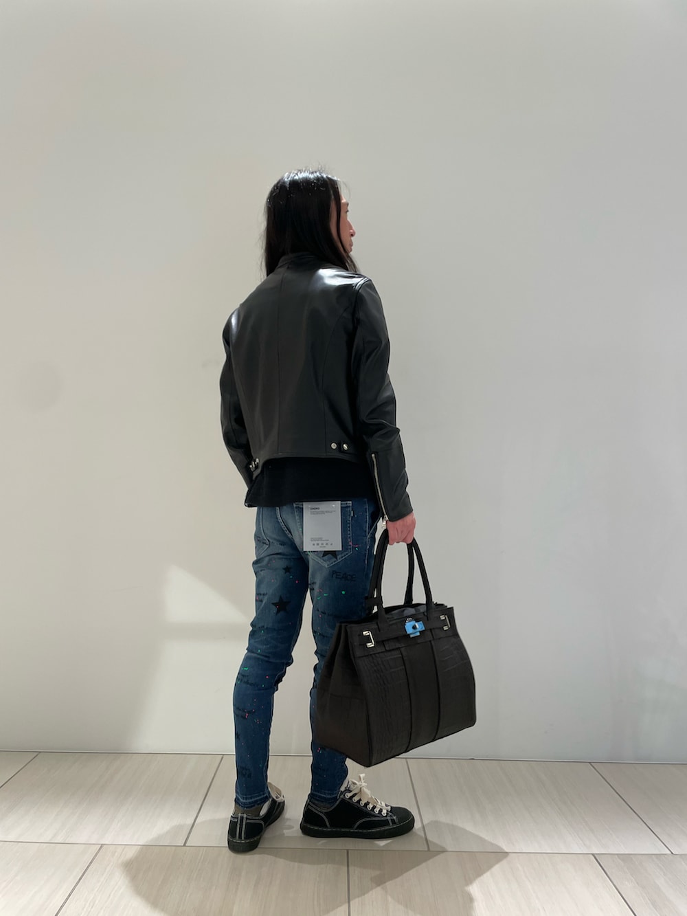 ブラック系のライダースジャケット、ブラック系のトートバッグ、ブルー系のデニムパンツを着用したメンズの秋コーディネートの2枚目の写真