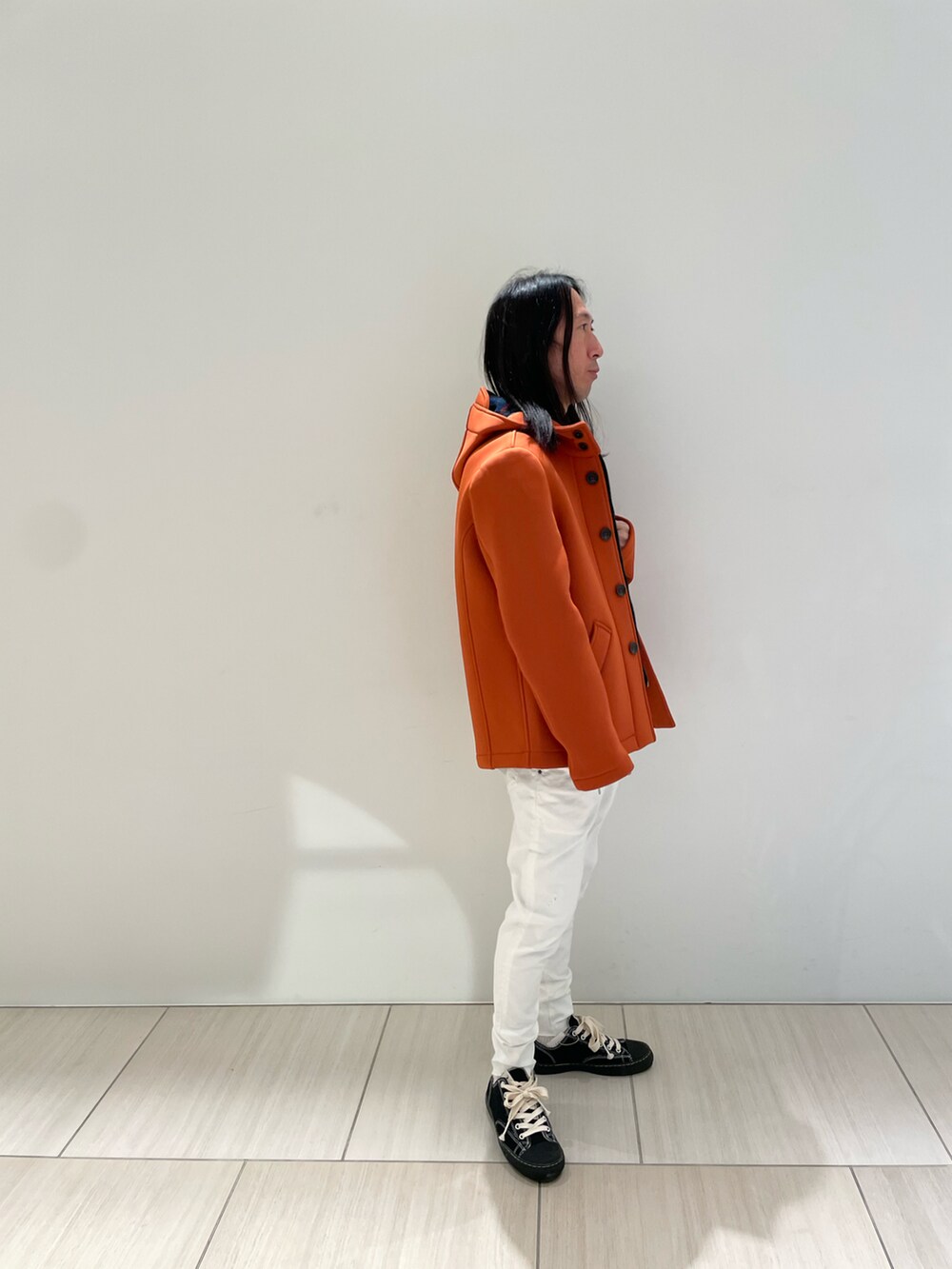 オレンジ系のブルゾン、ベージュ系のニット/セーター、ホワイト系のデニムパンツを着用したメンズの秋コーディネートの2枚目の写真