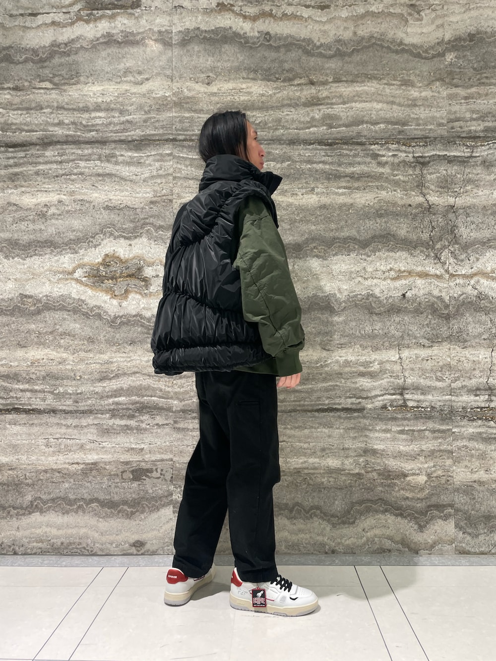 グリーン系のブルゾン、ブラック系のダウンベスト、ホワイト系のスニーカーを着用したメンズの冬コーディネートの4枚目の写真