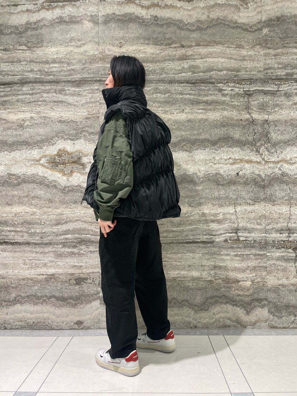 グリーン系のブルゾン、ブラック系のダウンベスト、ホワイト系のスニーカーを着用したメンズの冬コーディネートの3枚目の写真