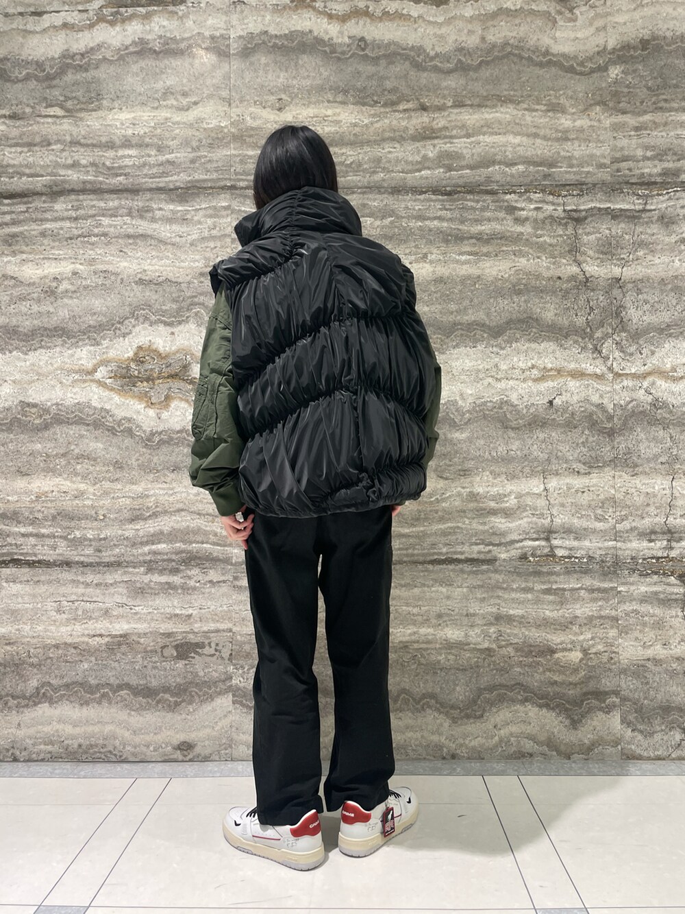 グリーン系のブルゾン、ブラック系のダウンベスト、ホワイト系のスニーカーを着用したメンズの冬コーディネートの2枚目の写真