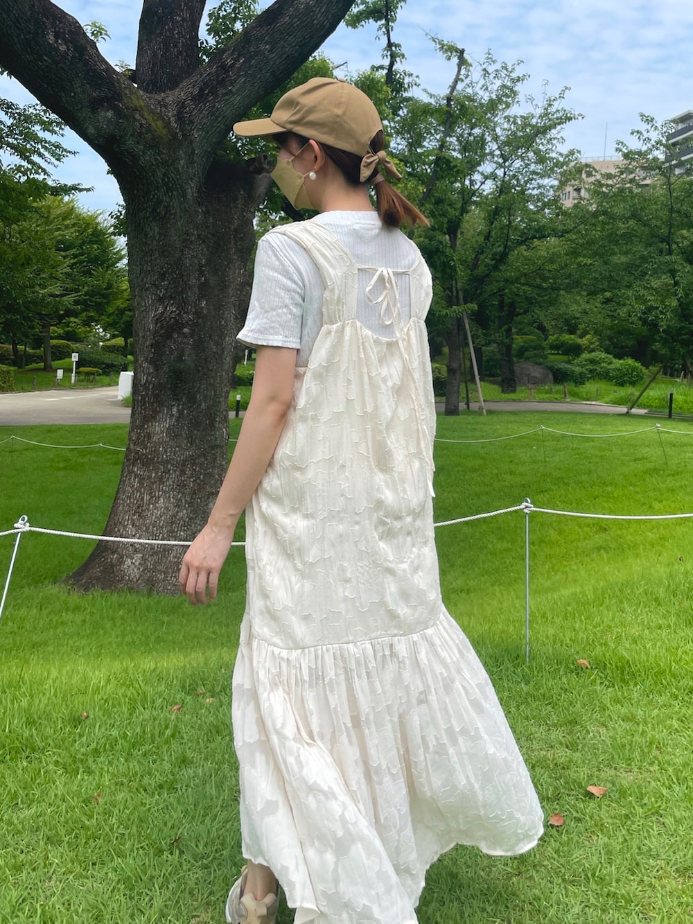 ホワイト系のワンピース、ベージュ系のスニーカー、ブラウン系のキャップを着用したレディースの夏コーディネートの2枚目の写真