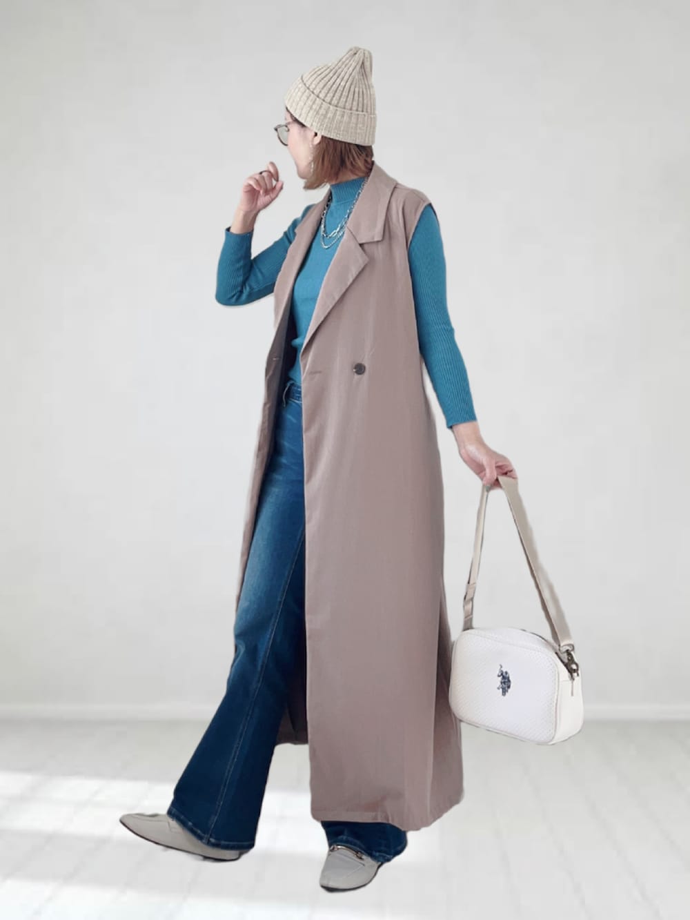 ブルー系のデニムパンツ、ベージュ系のベスト、ホワイト系のショルダーバッグを着用したレディースの春コーディネートの2枚目の写真