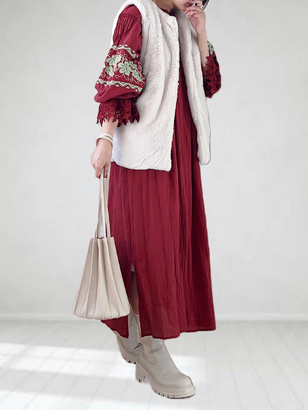 ホワイト系のブーツ、ホワイト系のベスト、レッド系のワンピースを着用したレディースの秋コーディネートの2枚目の写真