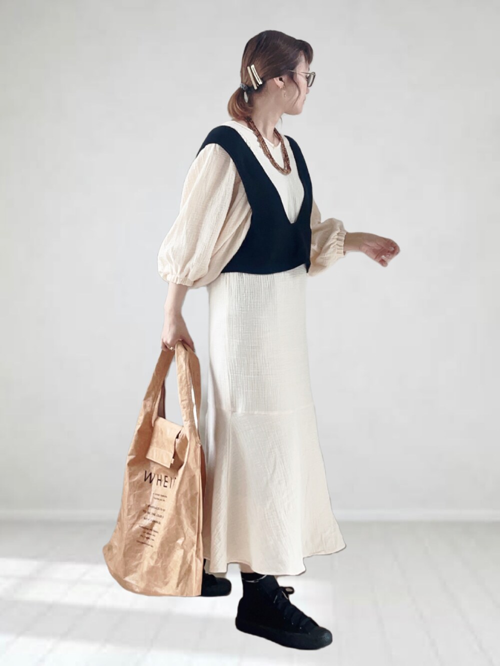 ホワイト系のワンピース、ブラック系のベスト、ベージュ系のトートバッグを着用したレディースの春コーディネートの2枚目の写真