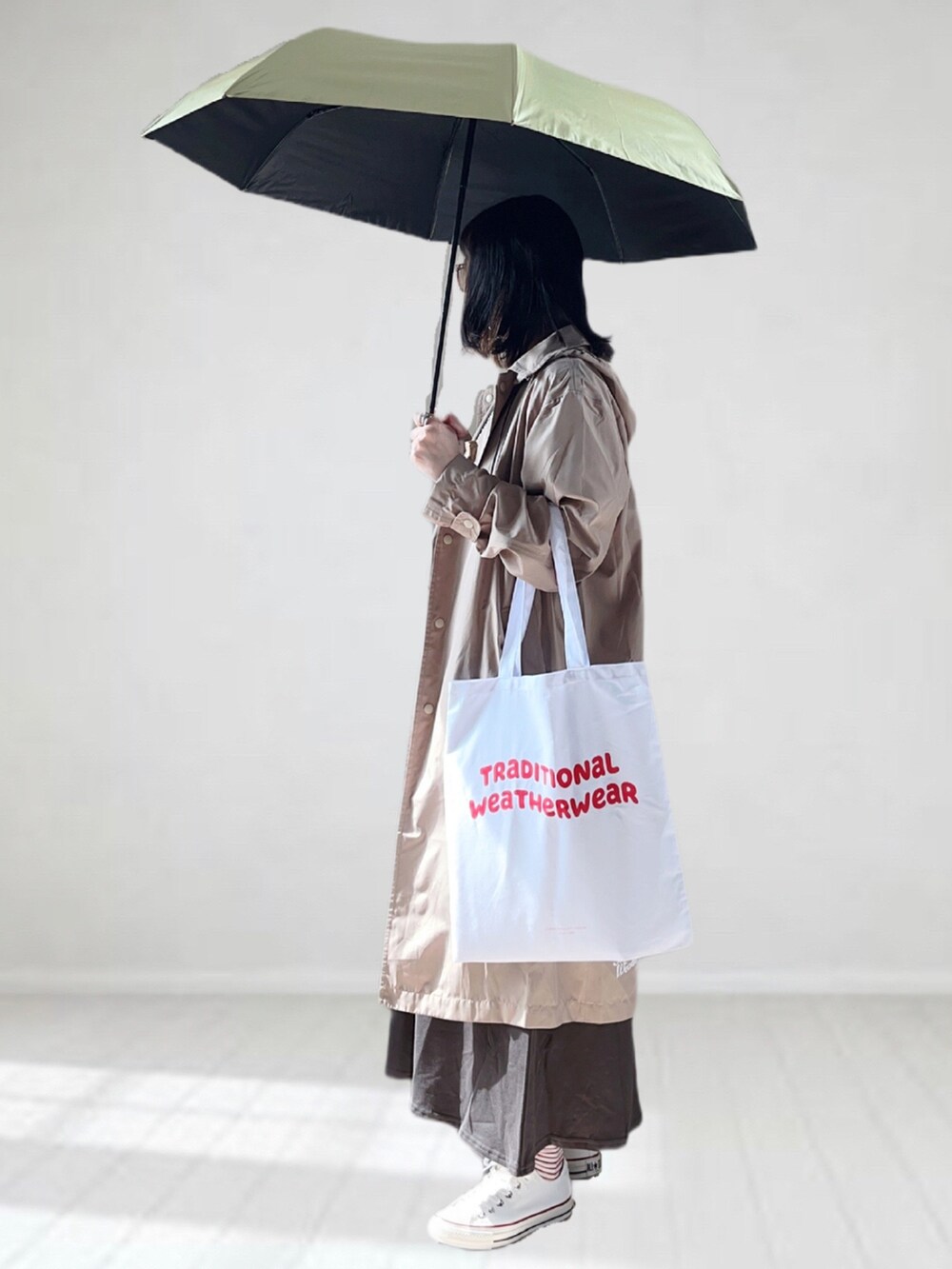 グレー系のワンピース、ホワイト系のスニーカー、ベージュ系のレインコート/ポンチョを着用したレディースの春コーディネートの2枚目の写真