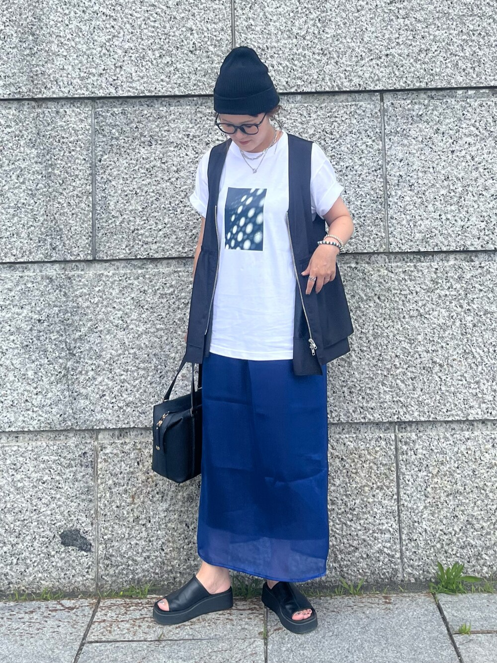 ブラック系のベスト、ブルー系のスカート、ブラック系のサンダルを着用したレディースの夏コーディネートの4枚目の写真