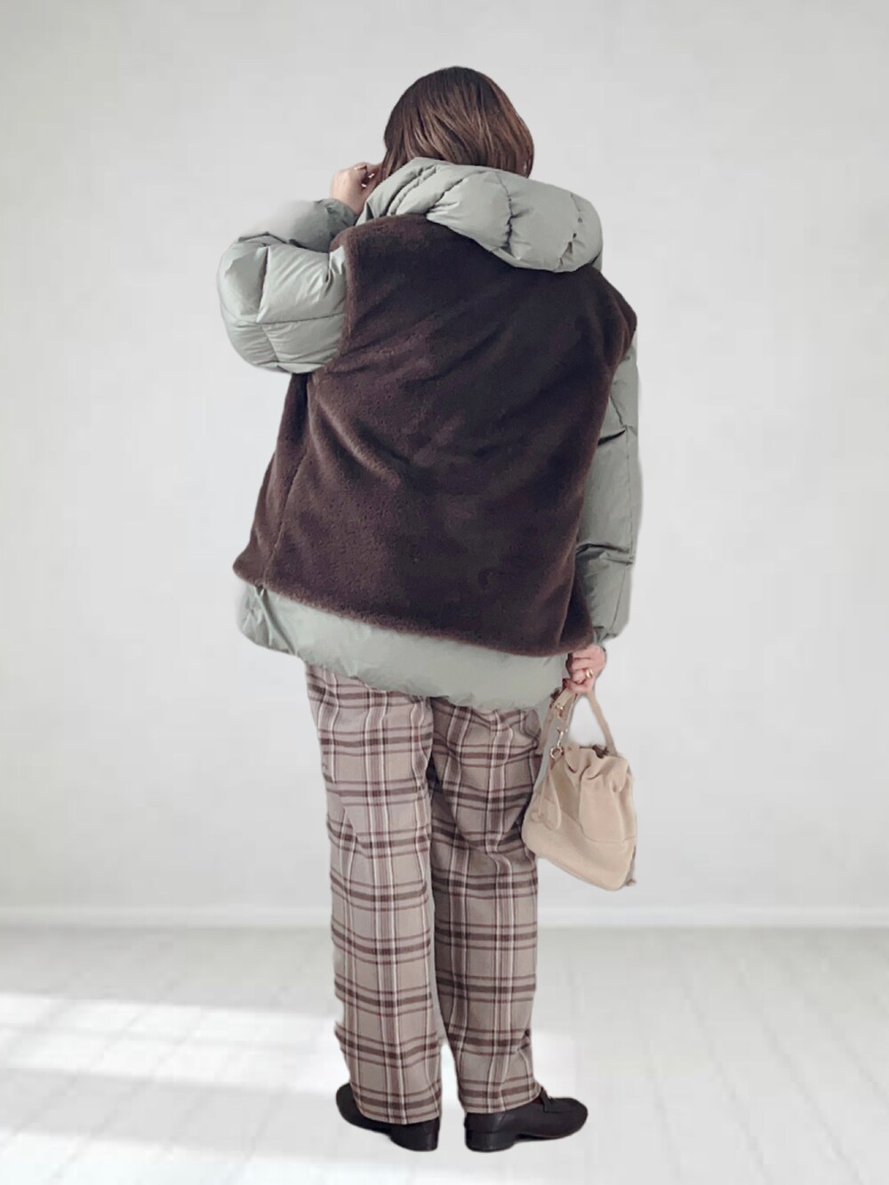 グリーン系のダウンジャケット/コート、ブラウン系のベスト、ホワイト系のニット/セーターを着用したレディースの冬コーディネートの2枚目の写真