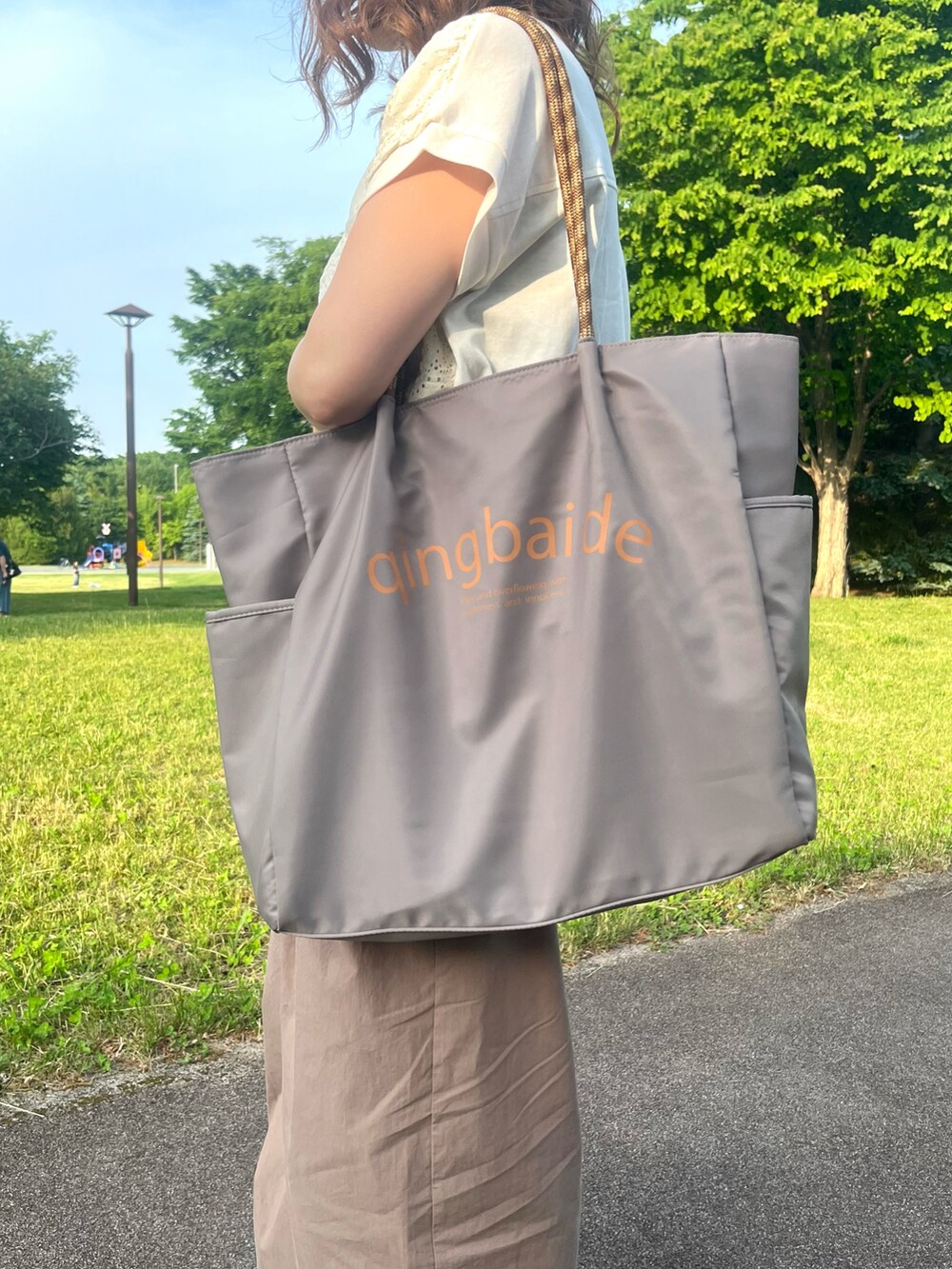 グレー系のトートバッグ、ホワイト系のTシャツ/カットソー、オレンジ系のスニーカーを着用したレディースの夏コーディネートの4枚目の写真