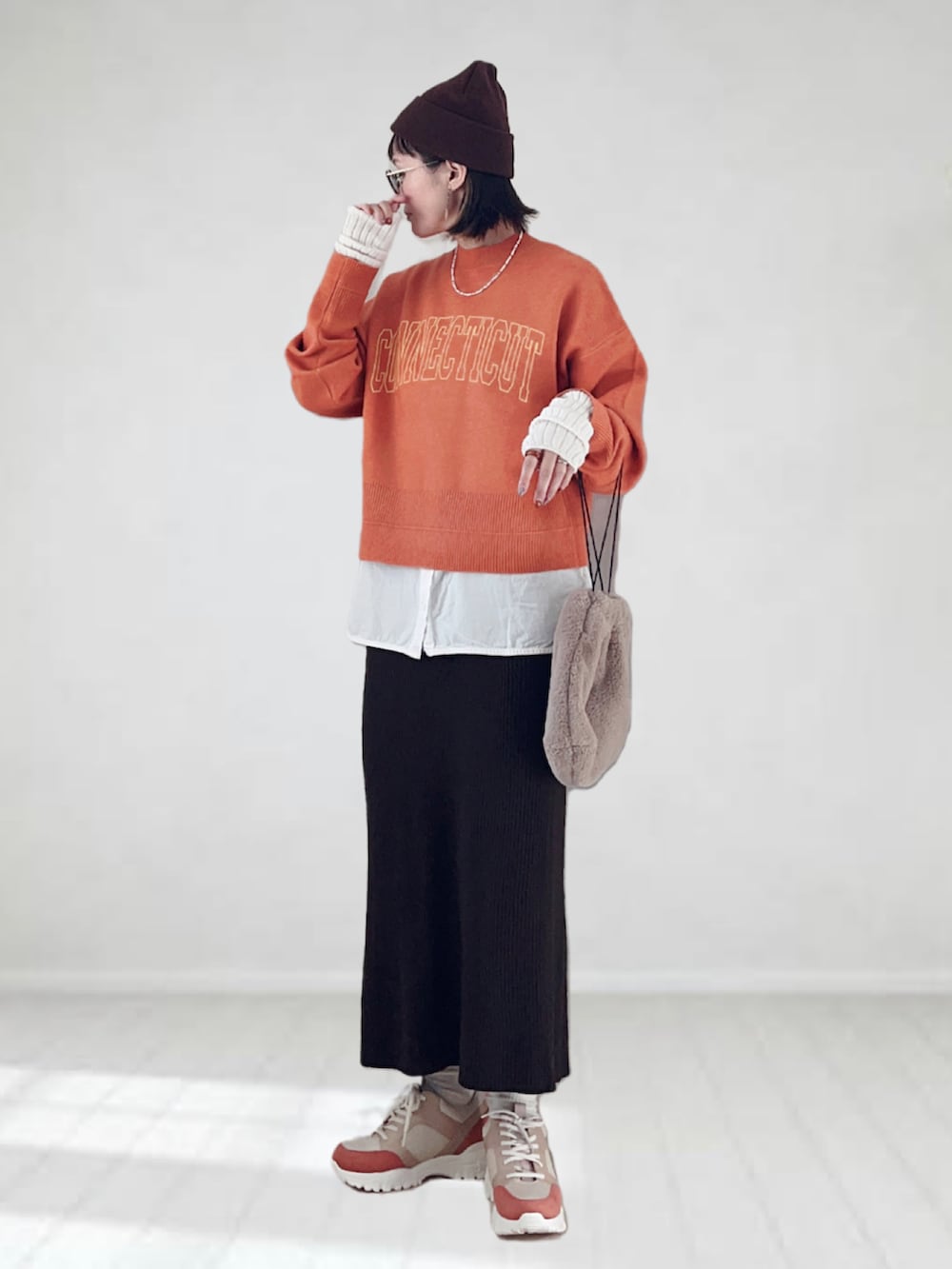 オレンジ系のニット/セーター、ホワイト系のタンクトップ、ブラウン系のスカートを着用したレディースの秋コーディネートの2枚目の写真