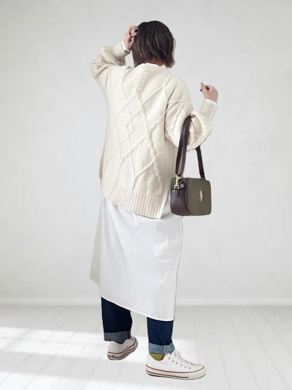 グリーン系のショルダーバッグ、グレー系のワンピース、ブルー系のデニムパンツを着用したレディースの冬コーディネートの2枚目の写真