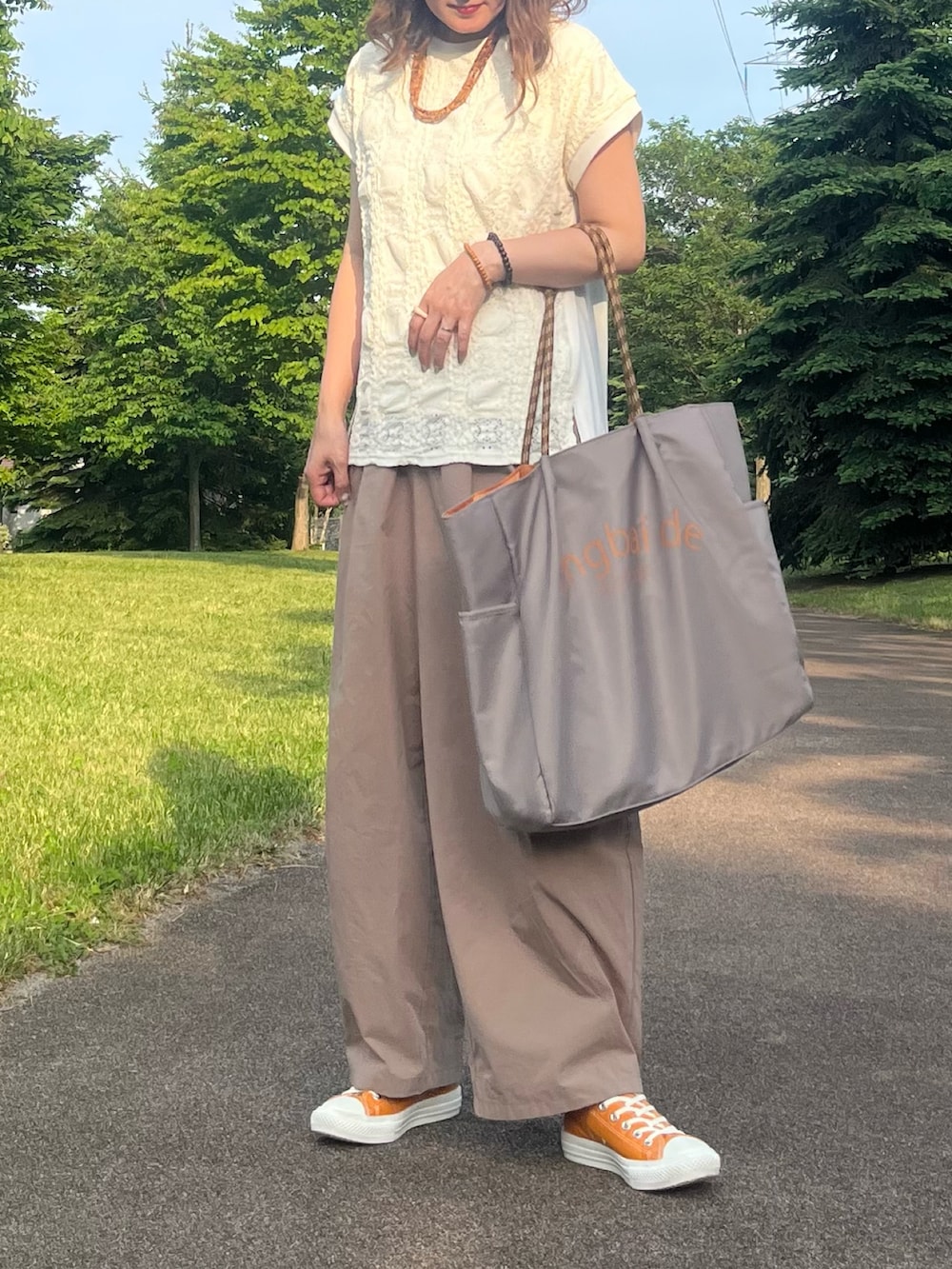 グレー系のトートバッグ、ホワイト系のTシャツ/カットソー、オレンジ系のスニーカーを着用したレディースの夏コーディネートの2枚目の写真