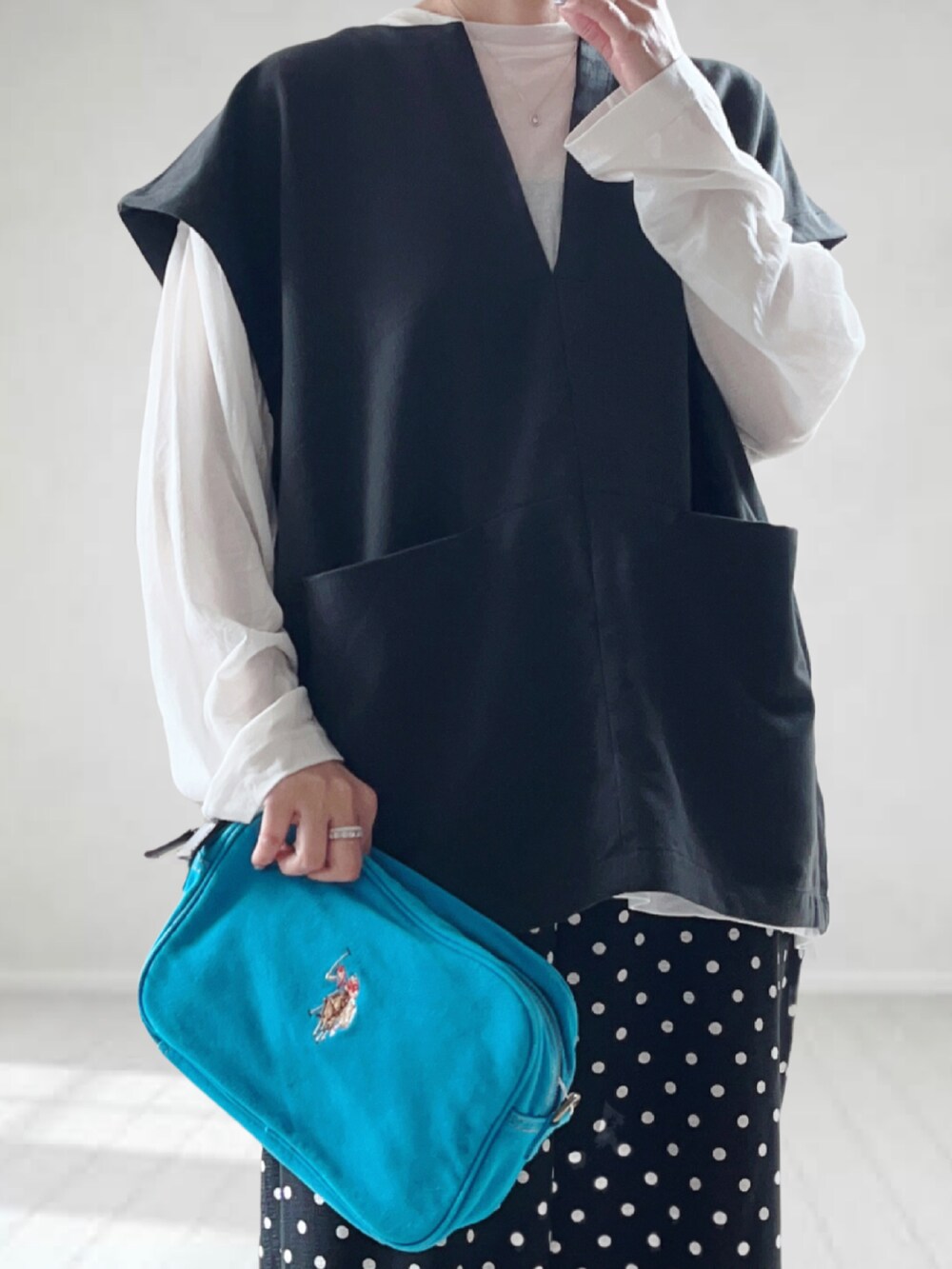 ブルー系のショルダーバッグ、ブラック系のベスト、ホワイト系のTシャツ/カットソーを着用したレディースの春コーディネートの2枚目の写真