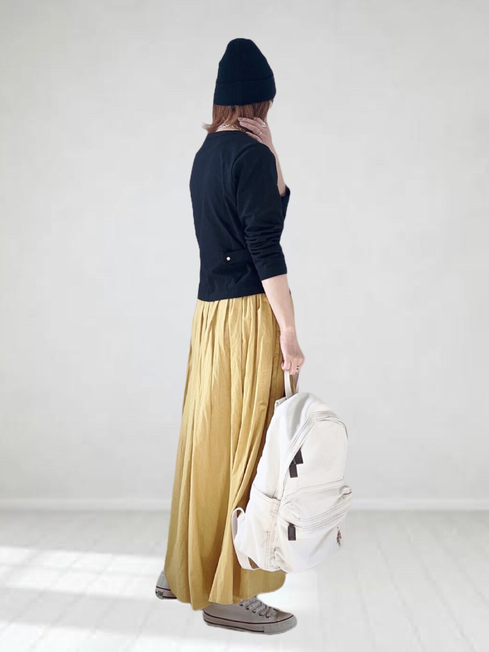 ブラック系のカーディガン/ボレロ、イエロー系のスカート、ホワイト系のバックパック/リュックを着用したレディースの春コーディネートの2枚目の写真