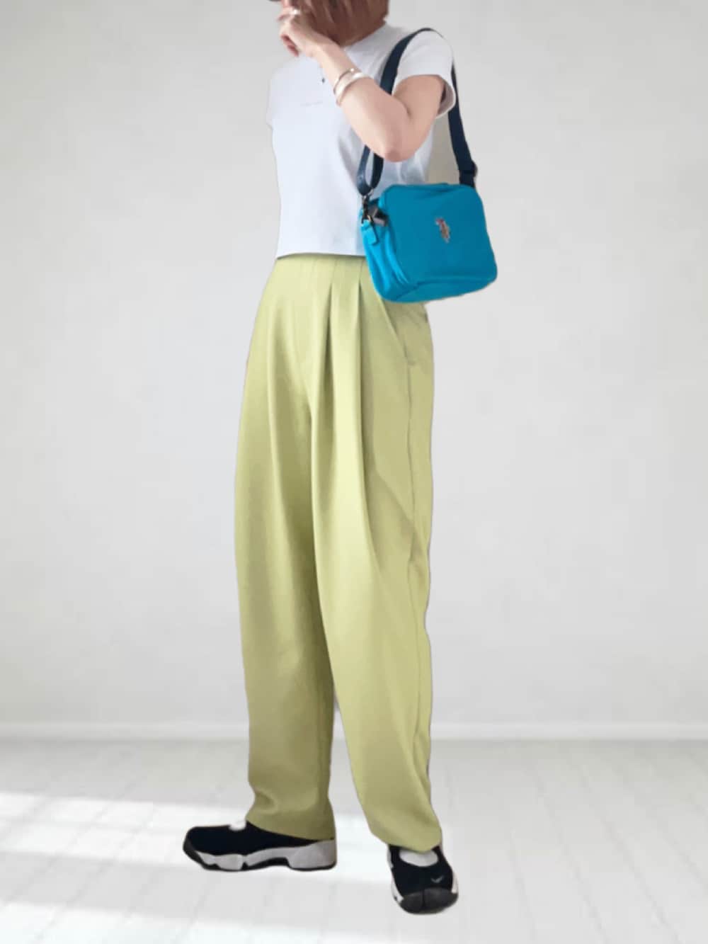 ブルー系のショルダーバッグ、ホワイト系のTシャツ/カットソー、イエロー系のスラックスを着用したレディースの春コーディネートの2枚目の写真