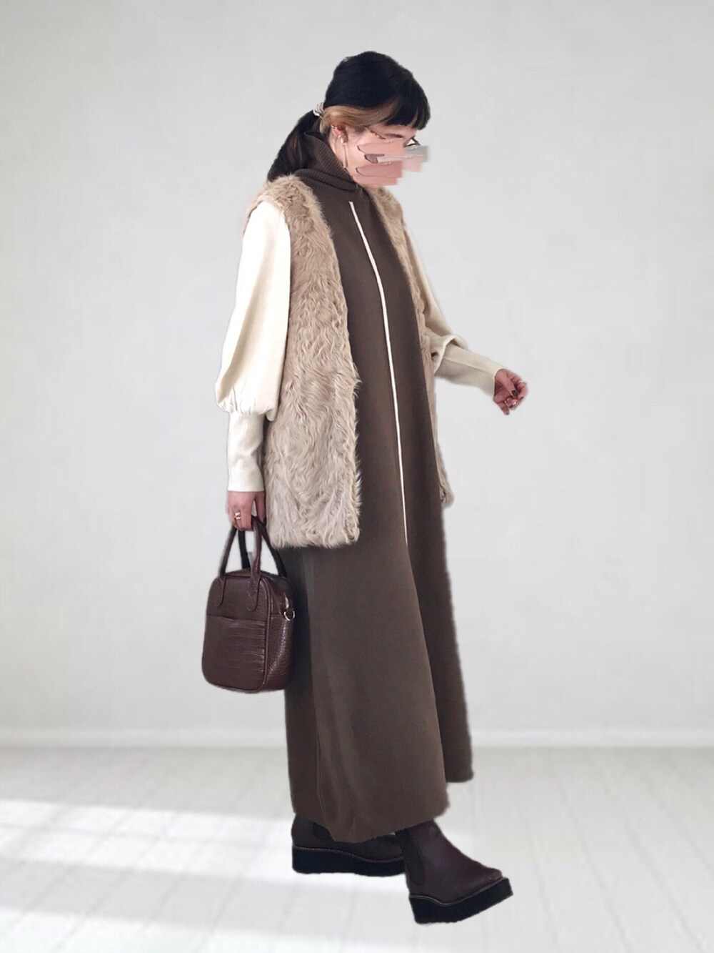 ブラウン系のワンピース、ベージュ系のベスト、ブラウン系のハンドバッグを着用したレディースの冬コーディネートの2枚目の写真