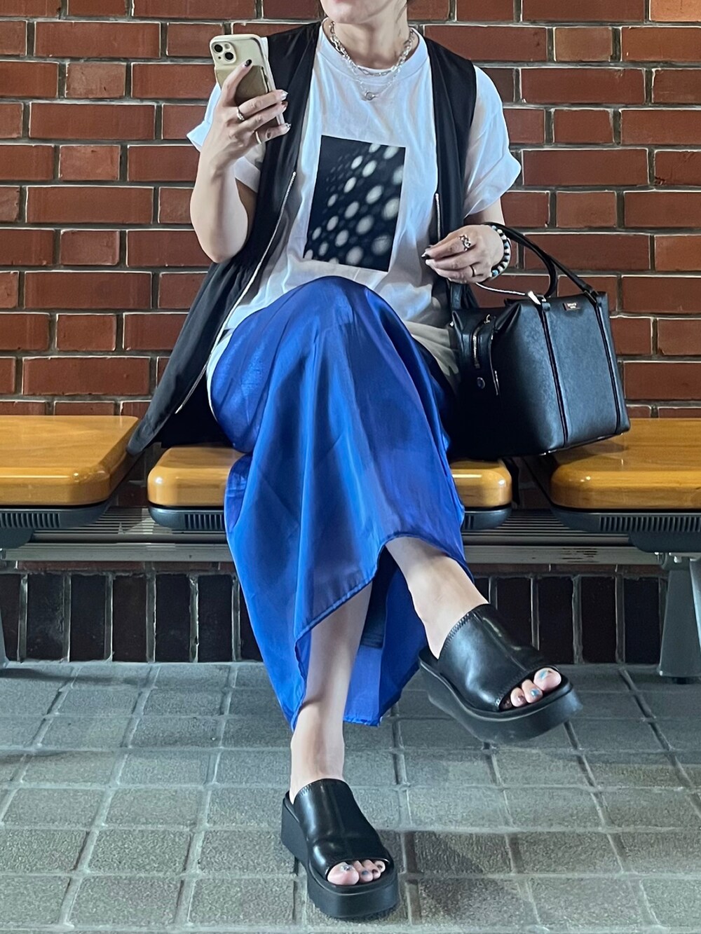 ブラック系のベスト、ブルー系のスカート、ブラック系のサンダルを着用したレディースの夏コーディネートの2枚目の写真