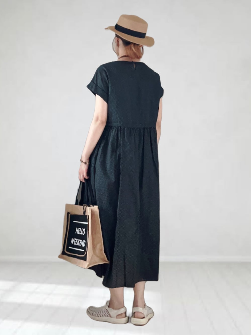 ブラック系のワンピース、ブラック系のかごバッグ、ホワイト系のサンダルを着用したレディースの夏コーディネートの2枚目の写真