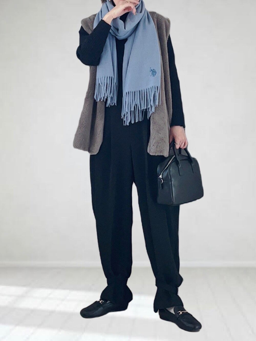 グレー系のベスト、ブラック系のボストンバッグ、ブラック系のローファーを着用したレディースの冬コーディネートの2枚目の写真