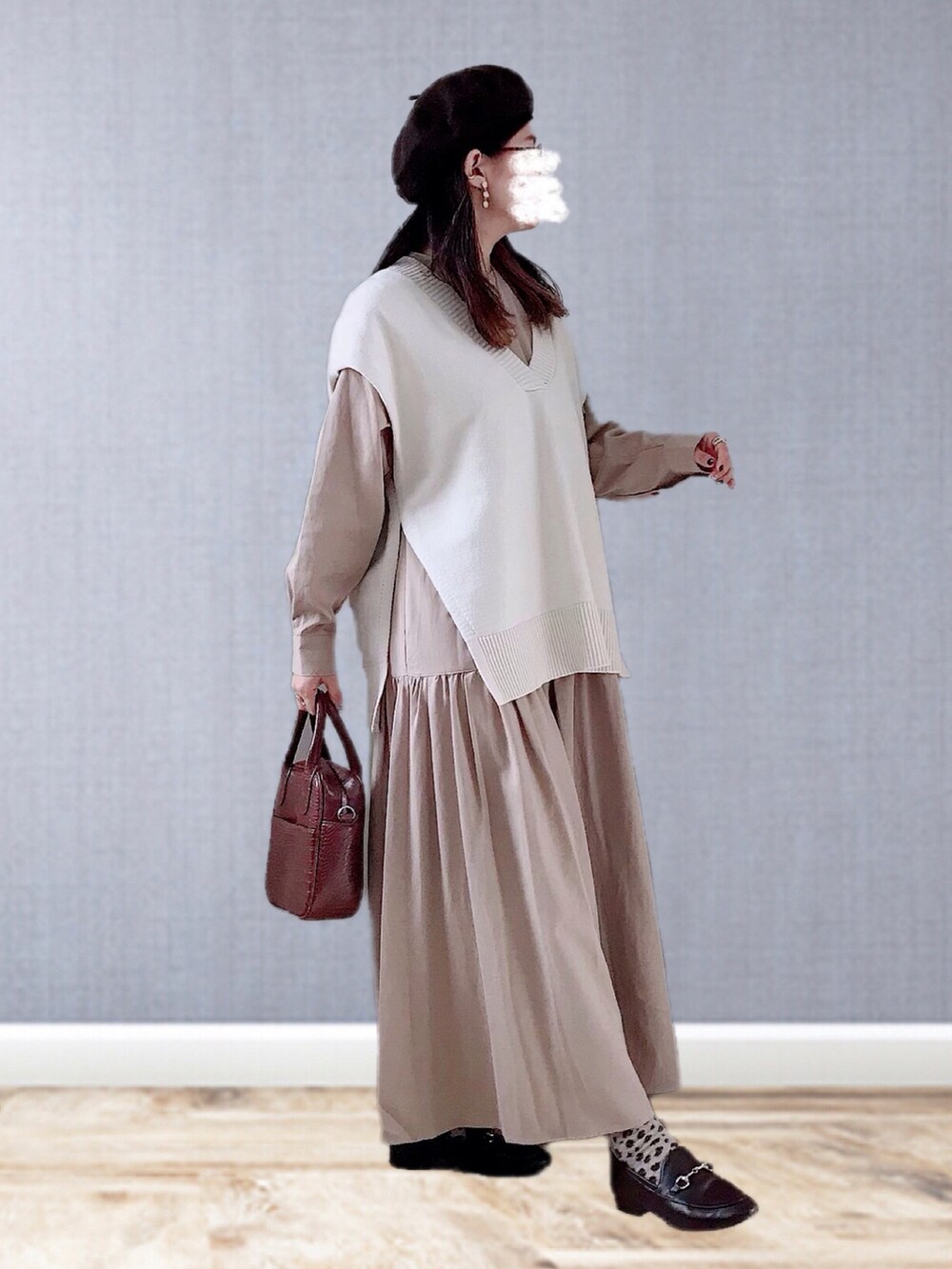 ベージュ系のワンピース、ホワイト系のベスト、ブラウン系のハンドバッグを着用したレディースの冬コーディネートの2枚目の写真