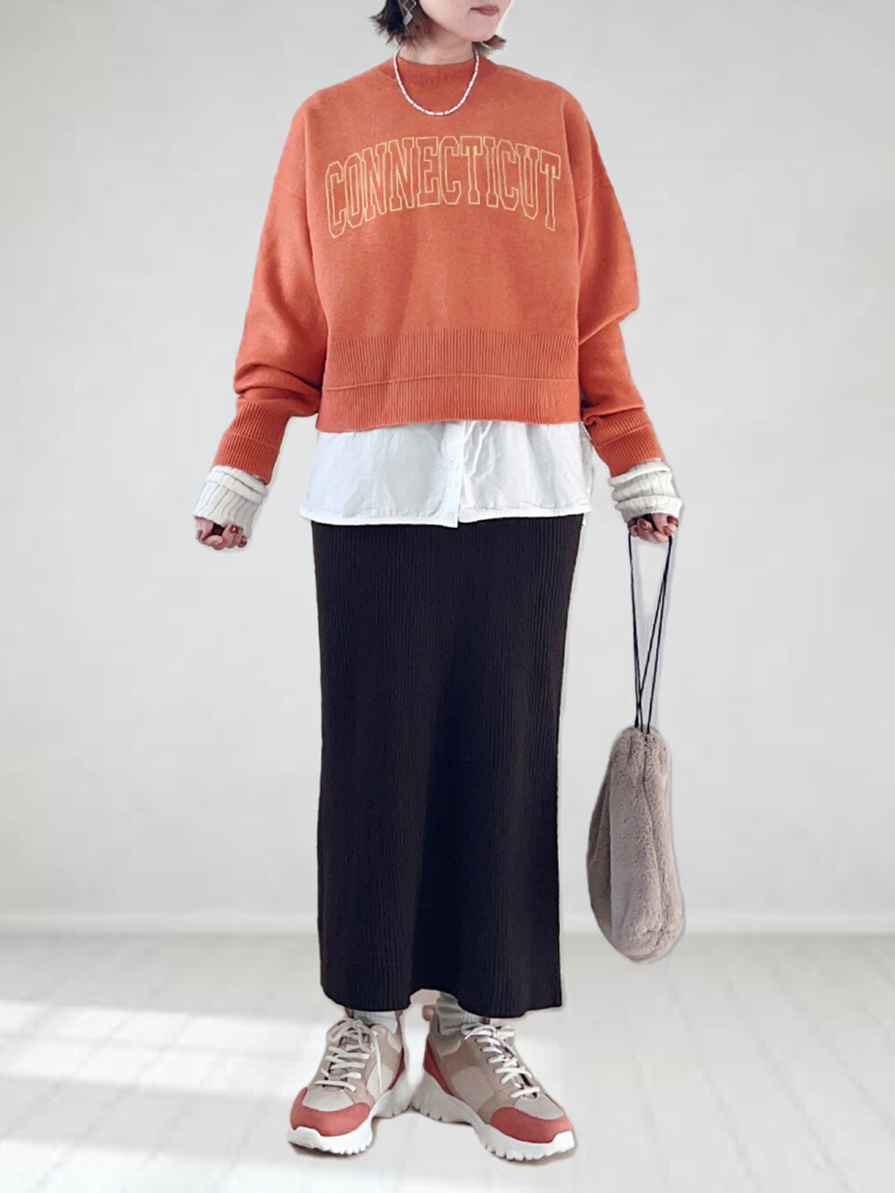 オレンジ系のニット/セーター、ホワイト系のタンクトップ、ブラウン系のスカートを着用したレディースの秋コーディネートの5枚目の写真