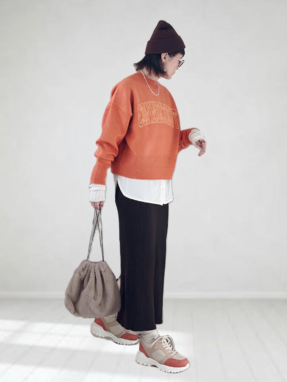 オレンジ系のニット/セーター、ホワイト系のタンクトップ、ブラウン系のスカートを着用したレディースの秋コーディネートの4枚目の写真