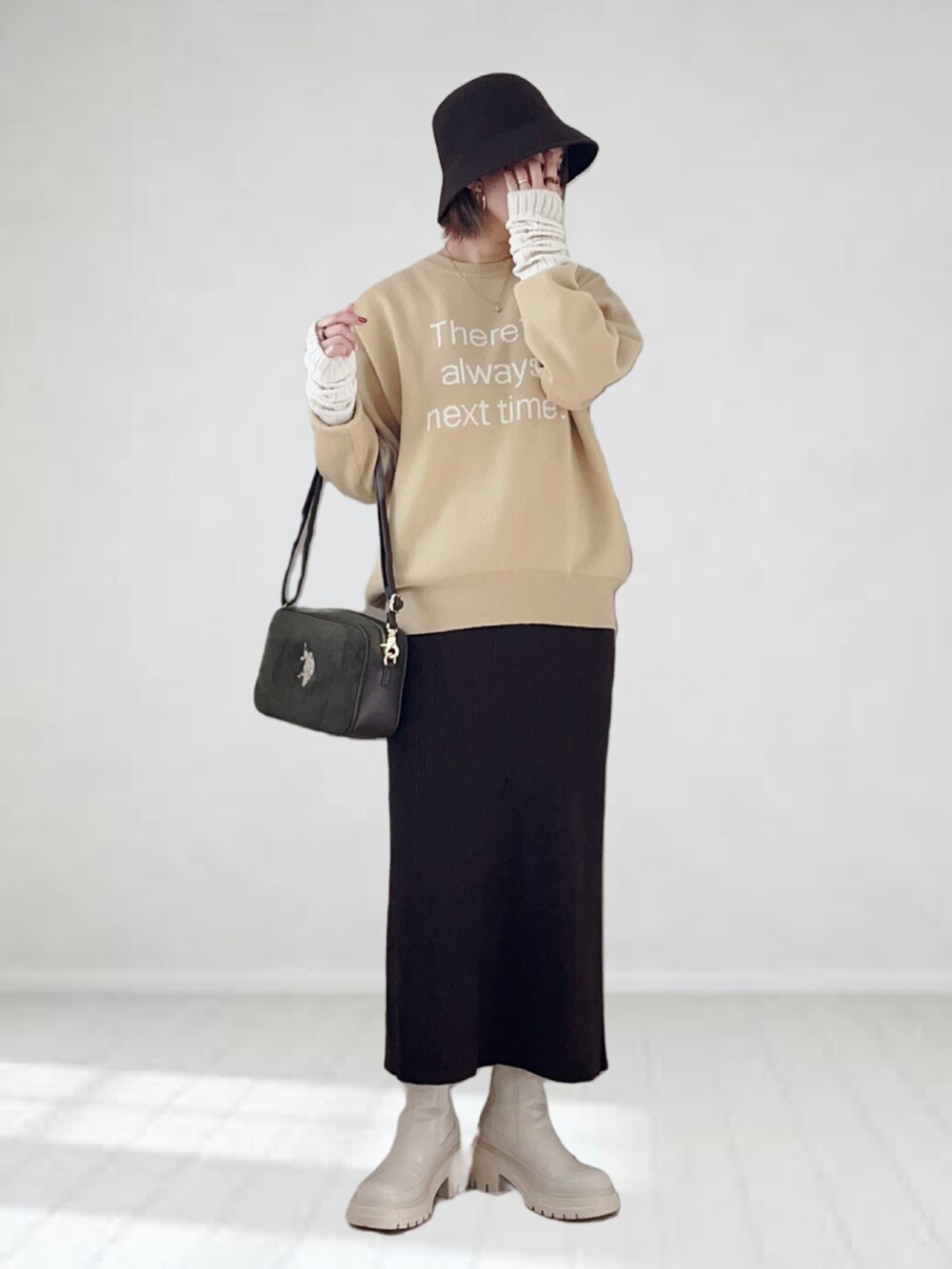 イエロー系のニット/セーター、グリーン系のショルダーバッグ、ブラウン系のスカートを着用したレディースの冬コーディネートの2枚目の写真