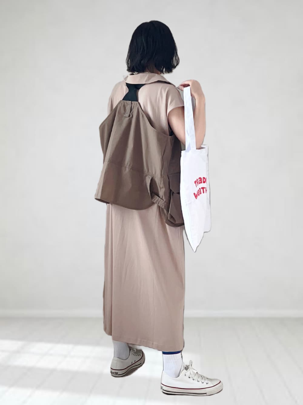 ベージュ系のワンピース、ブラウン系のベスト、レッド系のトートバッグを着用したレディースの夏コーディネートの2枚目の写真