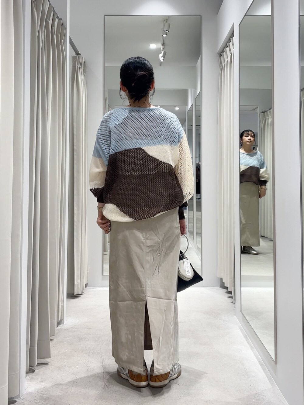 ブルー系のニット/セーター、ベージュ系のスカート、ブラック系のハンドバッグを着用したレディースの秋コーディネートの4枚目の写真